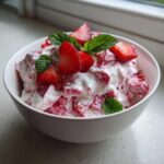 Nahaufnahme von cremigem Erdbeer-Quark mit frischen Erdbeerstücken und Minze in einer weißen Schale.