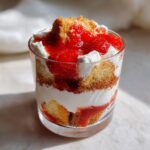 Nahaufnahme von einem geschichteten Erdbeer-Tiramisu im Glas mit Biskuit, Sahne und Erdbeersoße.