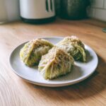Drei fertige Kohlknödel auf einem hellen Teller, bestreut mit gerösteten Semmelbröseln.