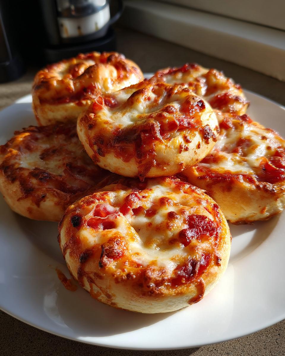 Fünf goldbraune Pizzabrötchen mit geschmolzenem Käse und Tomatensauce auf einem weißen Teller.