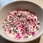 Nahaufnahme eines cremigen Radieschen-Dips mit leuchtend rosa Radieschenstücken und Schnittlauch in einer weißen Schüssel.