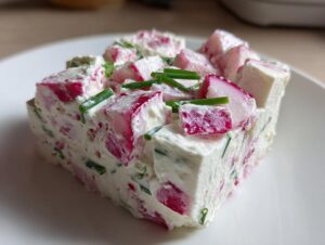 Nahaufnahme eines festen Blocks Radieschen-Dip mit großen Radieschenstücken und Schnittlauch auf einem weißen Teller.