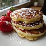 Stapel von fluffige Quarkpfannkuchen, bestäubt mit Puderzucker und garniert mit frischen Erdbeeren.