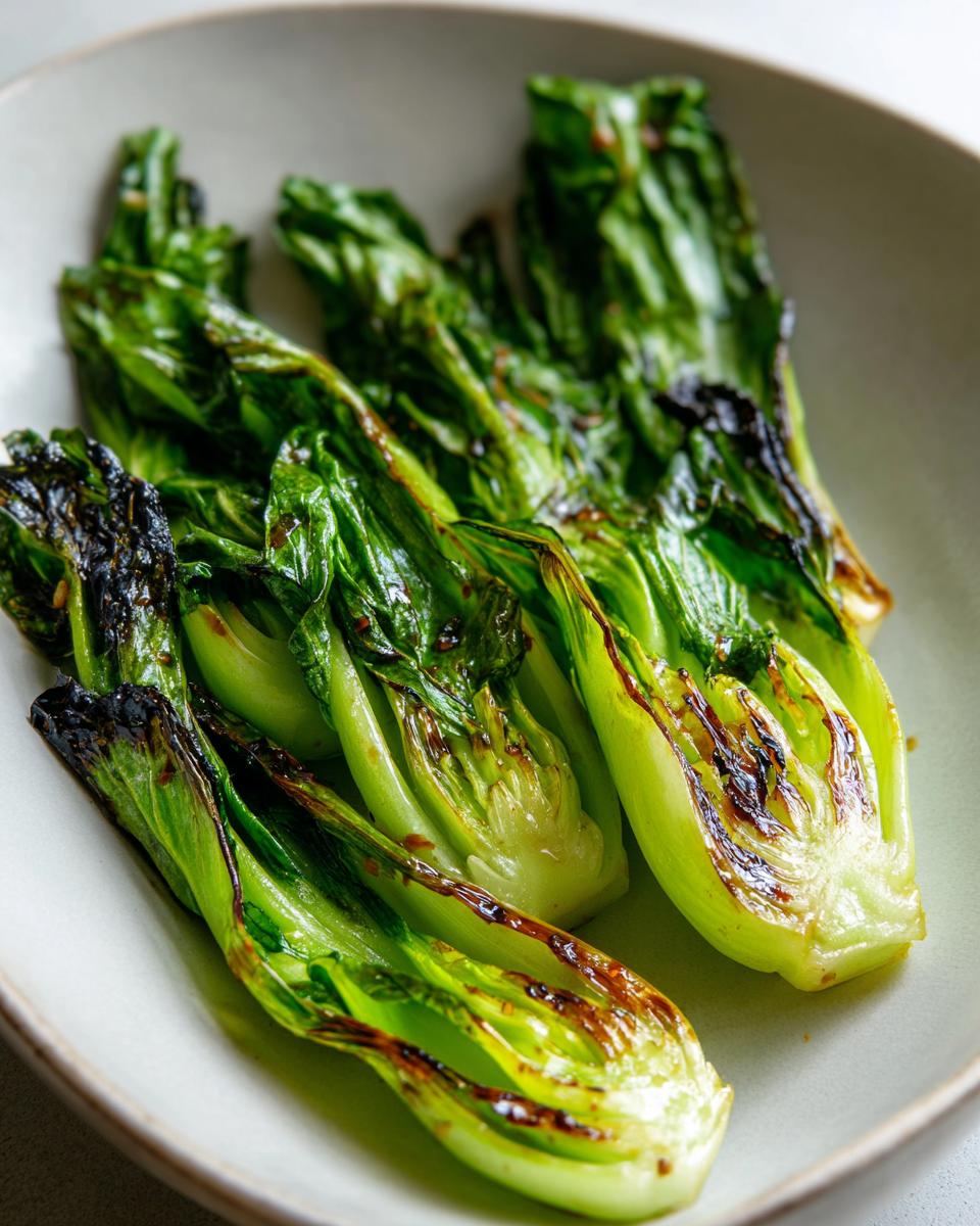 Nahaufnahme von perfekt gebratenem Pak Choi mit leicht karamellisierten Rändern auf einem hellen Teller.