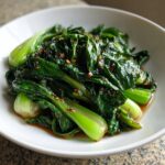 Nahaufnahme von saftigem, gebratenem Pak Choi in der Pfanne in einer weißen Schüssel mit dunkler Soße.