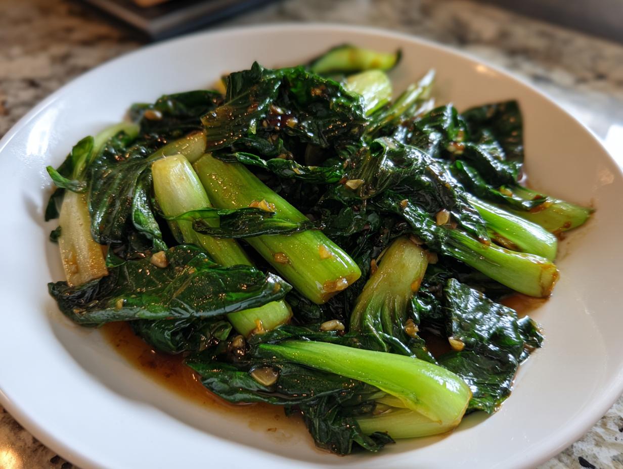 Nahaufnahme von saftigem, gebratenem Pak Choi in der Pfanne mit dunkler Soße auf einem weißen Teller.