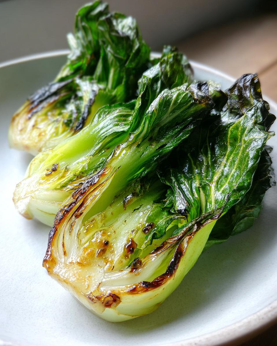 Drei Hälften von Gebratener Pak Choi mit leicht karamellisierten Rändern auf einem hellen Teller.