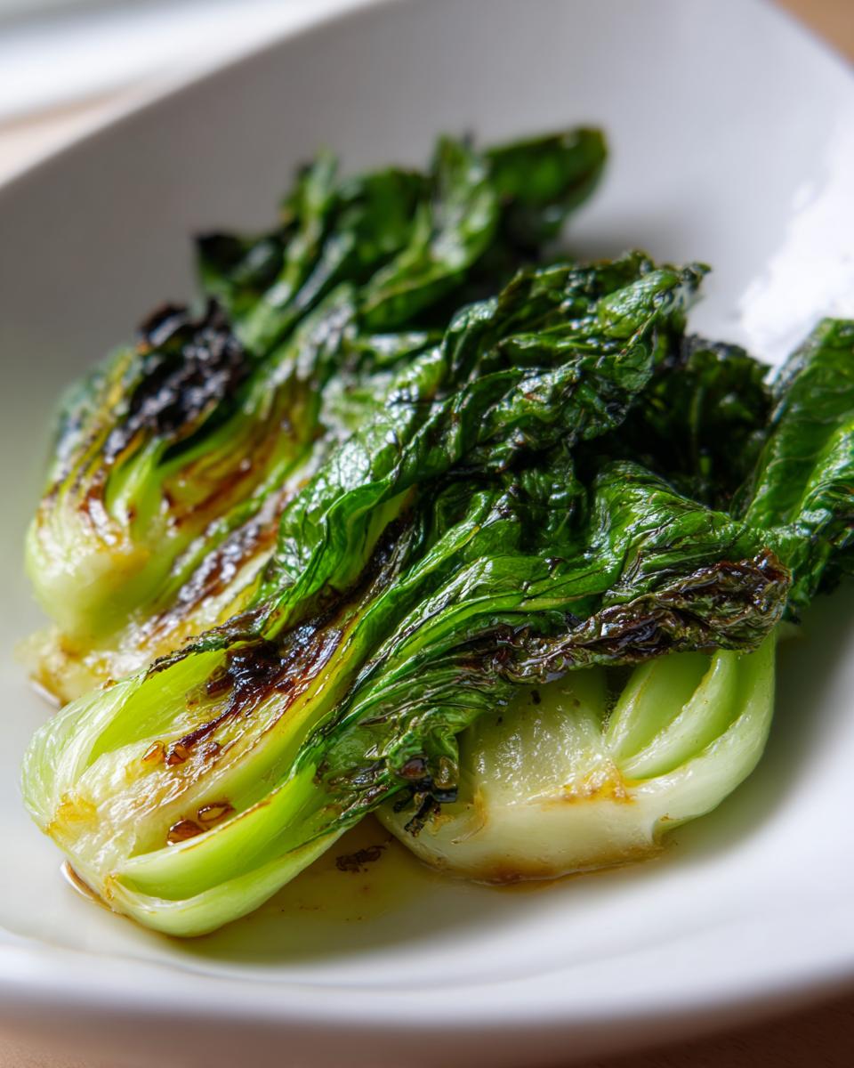 Nahaufnahme von perfekt gebratenem Pak Choi mit leicht karamellisierten Rändern auf einem weißen Teller.