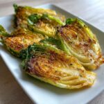 Vier Hälften von gebratenem Spitzkohl, goldbraun und mit Parmesan bestreut, auf einem weißen Teller.