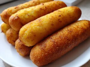 Nahaufnahme von mehreren goldbraun frittierten Corn Dogs, die auf einem weißen Teller gestapelt sind.