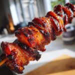 Nahaufnahme von saftigen, karamellisierten Grillfackeln aus Schweinebauch auf einem Holzspieß.