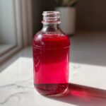 Eine Glasflasche gefüllt mit intensiv pinkem Rhabarbersirup, beleuchtet durch Sonnenlicht.