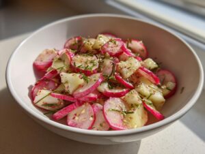 Nahaufnahme eines knackigen Radieschensalat mit Gurkenstücken und frischen Kräutern in einer weißen Schüssel.