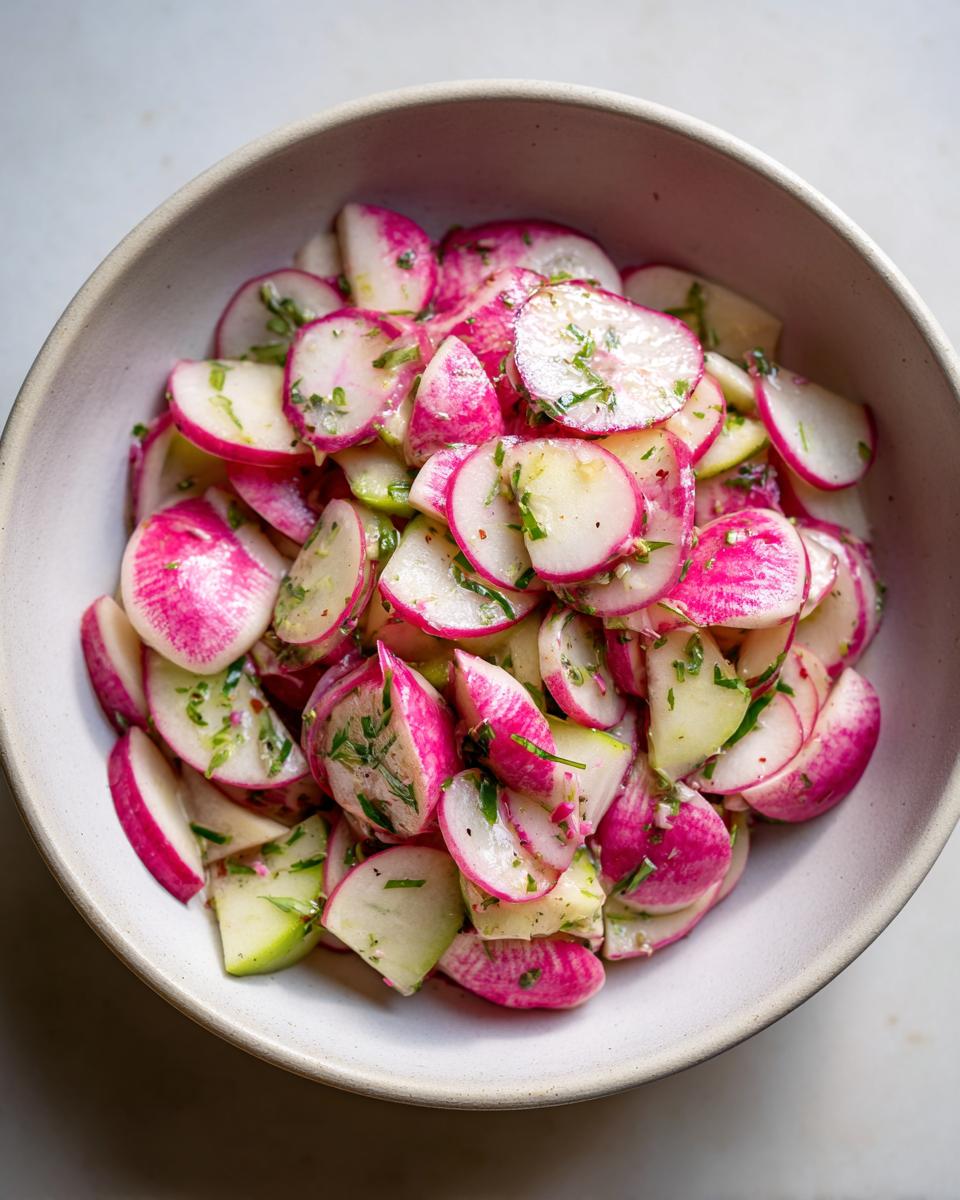 Nahaufnahme eines knackigen Radieschensalats mit rosa und weißen Radieschenscheiben und Kräutern in einer hellen Schale.