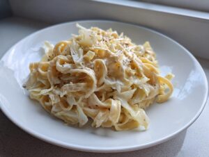 Nahaufnahme von cremigem Kohl-Alfredo mit breiten Nudeln, bestreut mit schwarzem Pfeffer auf einem weißen Teller.