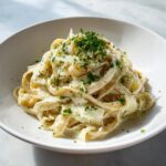 Nahaufnahme von cremigem Kohl-Alfredo mit Bandnudeln, garniert mit Petersilie und Parmesan.