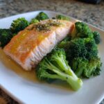 Nahaufnahme von saftigem Lachs mit Brokkoli, beträufelt mit Kräutern und Zitronensaft.