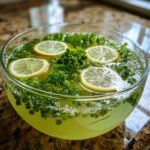 Nahaufnahme einer großen Glasschale mit leuchtend grüner Maibowle, garniert mit Zitronenscheiben und frischen Waldmeisterkräutern.