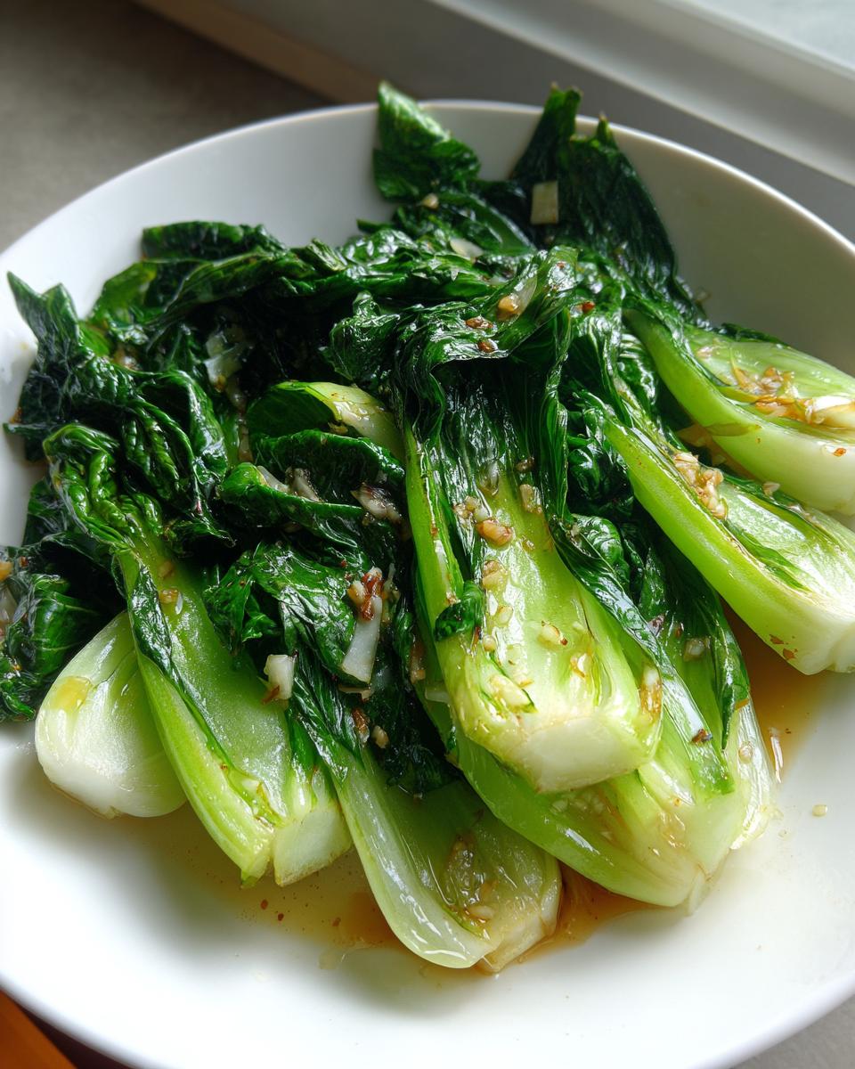 Nahaufnahme von frisch gebratenem Pak Choi mit sichtbaren Knoblauchstücken in einer hellen Soße.
