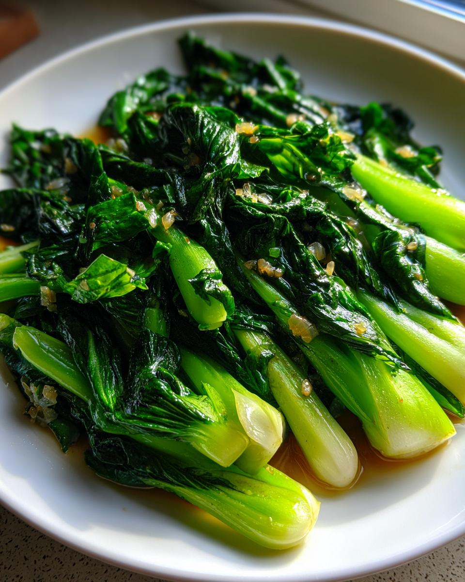 Nahaufnahme von leuchtend grünem, gebratenem Pak Choi mit sichtbaren Knoblauchstücken auf einem weißen Teller.