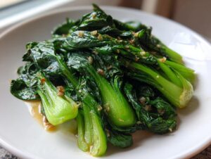 Nahaufnahme von leuchtend grünem, gebratenem Pak Choi mit Knoblauchstückchen auf einem weißen Teller.