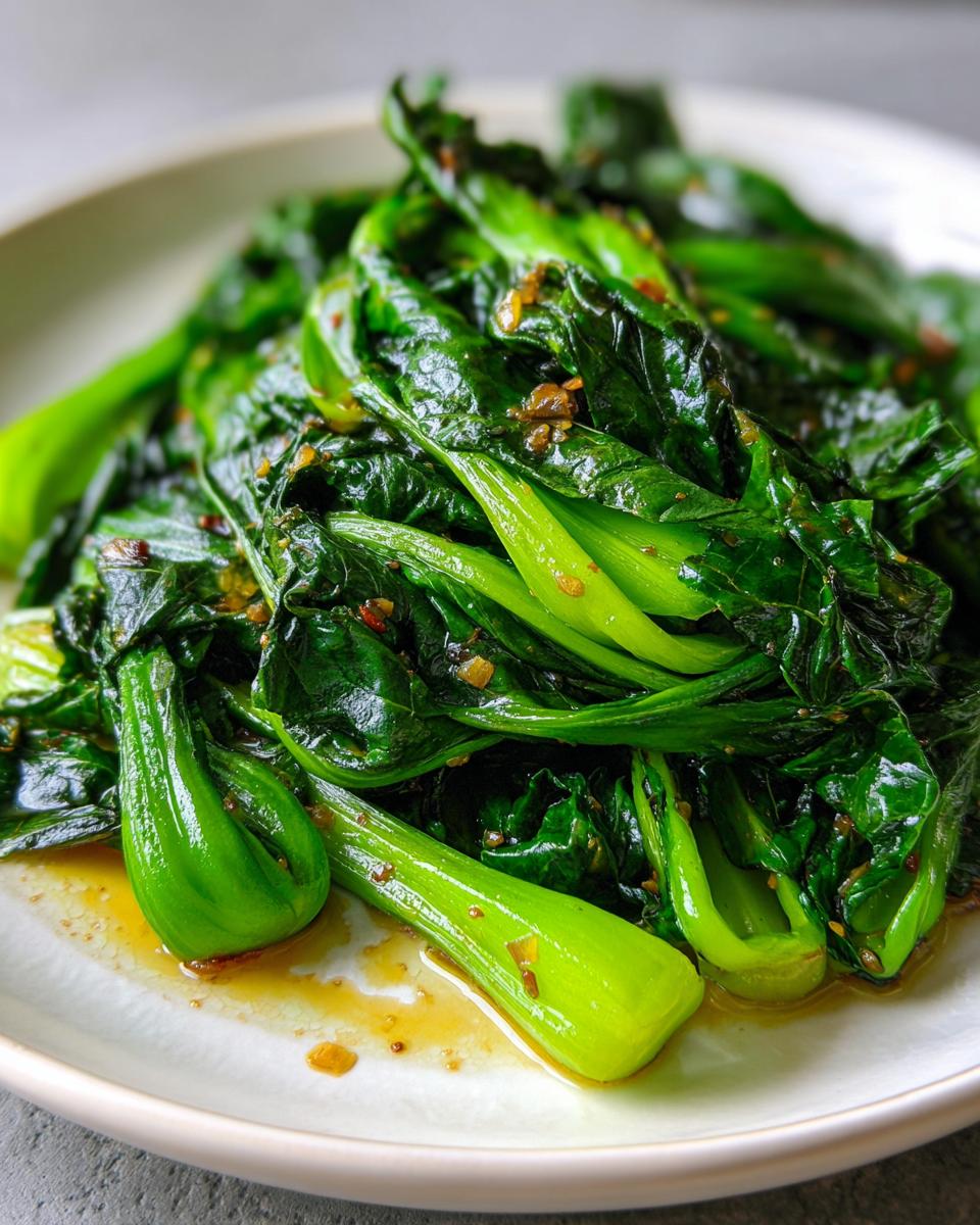 Nahaufnahme von leuchtend grünem, gebratenem Pak Choi mit einer leichten Soße auf einem weißen Teller.