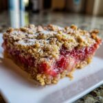 Nahaufnahme eines Stücks Rhabarber-Crumble mit knuspriger Streuseldecke auf einem weißen Teller.
