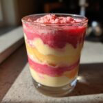 Geschichtetes Rhabarber Dessert mit Bananensahne in einem Glas, leuchtend rot und gelb.