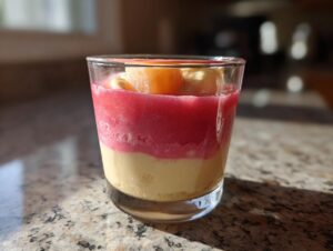 Geschichtetes Rhabarber Dessert mit Bananensahne in einem Glas, garniert mit Fruchtstücken.