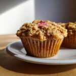 Ein einzelner, frisch gebackener Rhabarber-Muffin mit knusprigen Zimtstreuseln auf einem weißen Teller.
