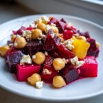 Nahaufnahme eines leuchtend roten Rote Bete Salat mit Kichererbsen und zerbröseltem Feta auf einem weißen Teller.