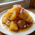 Nahaufnahme von goldgelbem Schwäbischer Kartoffelsalat mit Essig-Öl-Dressing und roten Zwiebelwürfeln auf einem weißen Teller.