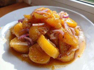 Nahaufnahme von Schwäbischer Kartoffelsalat mit Kartoffelstücken in Brühe und roten Zwiebelringen.