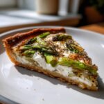 Nahaufnahme eines Stücks Spargel Flammkuchen mit Creme fraiche auf einem weißen Teller.