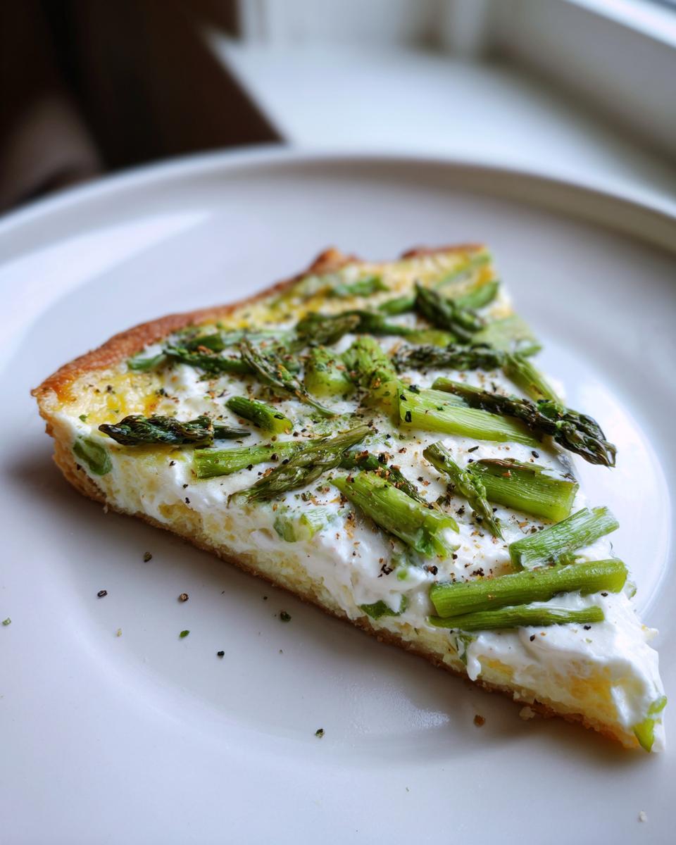 Nahaufnahme eines Stücks Spargel Flammkuchen mit Creme fraiche und grünem Spargel auf einem weißen Teller.