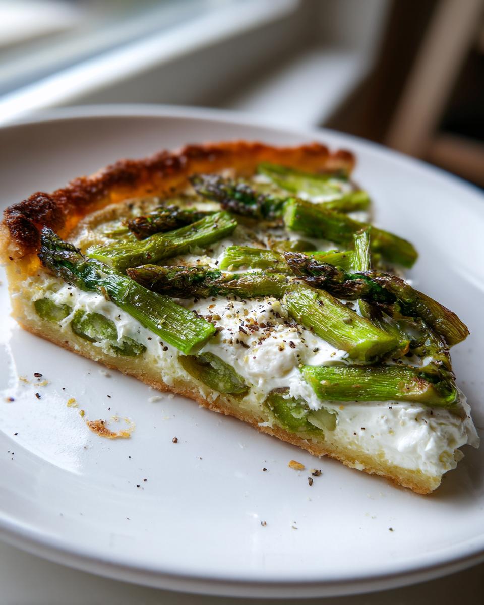 Nahaufnahme eines Stücks Spargel Flammkuchen mit Creme fraiche auf einem weißen Teller.