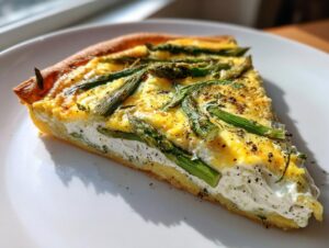 Ein Stück köstlicher Spargel Flammkuchen mit Creme fraiche und grünem Spargel auf einem weißen Teller.