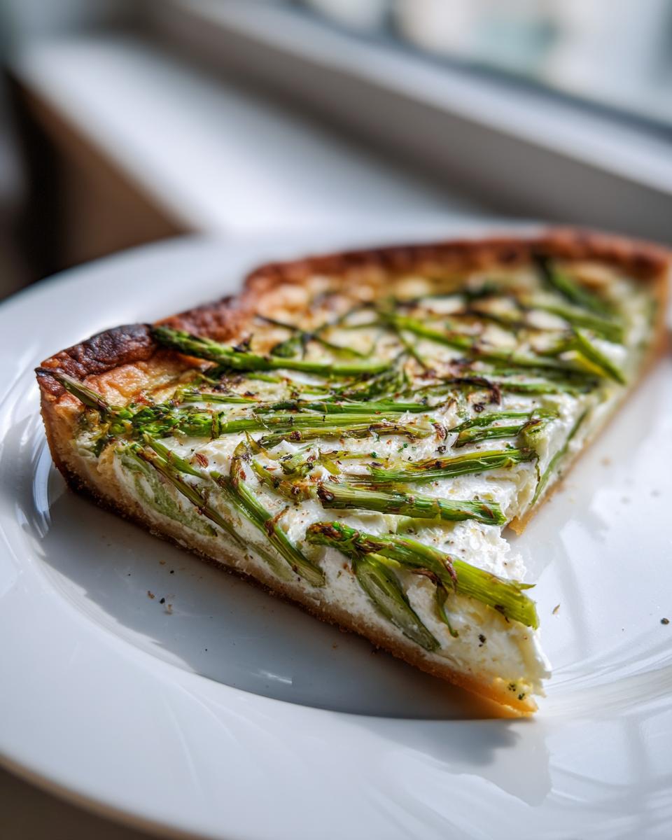 Nahaufnahme eines Stücks Spargel Flammkuchen mit Creme fraiche und grünem Spargel auf einem weißen Teller.