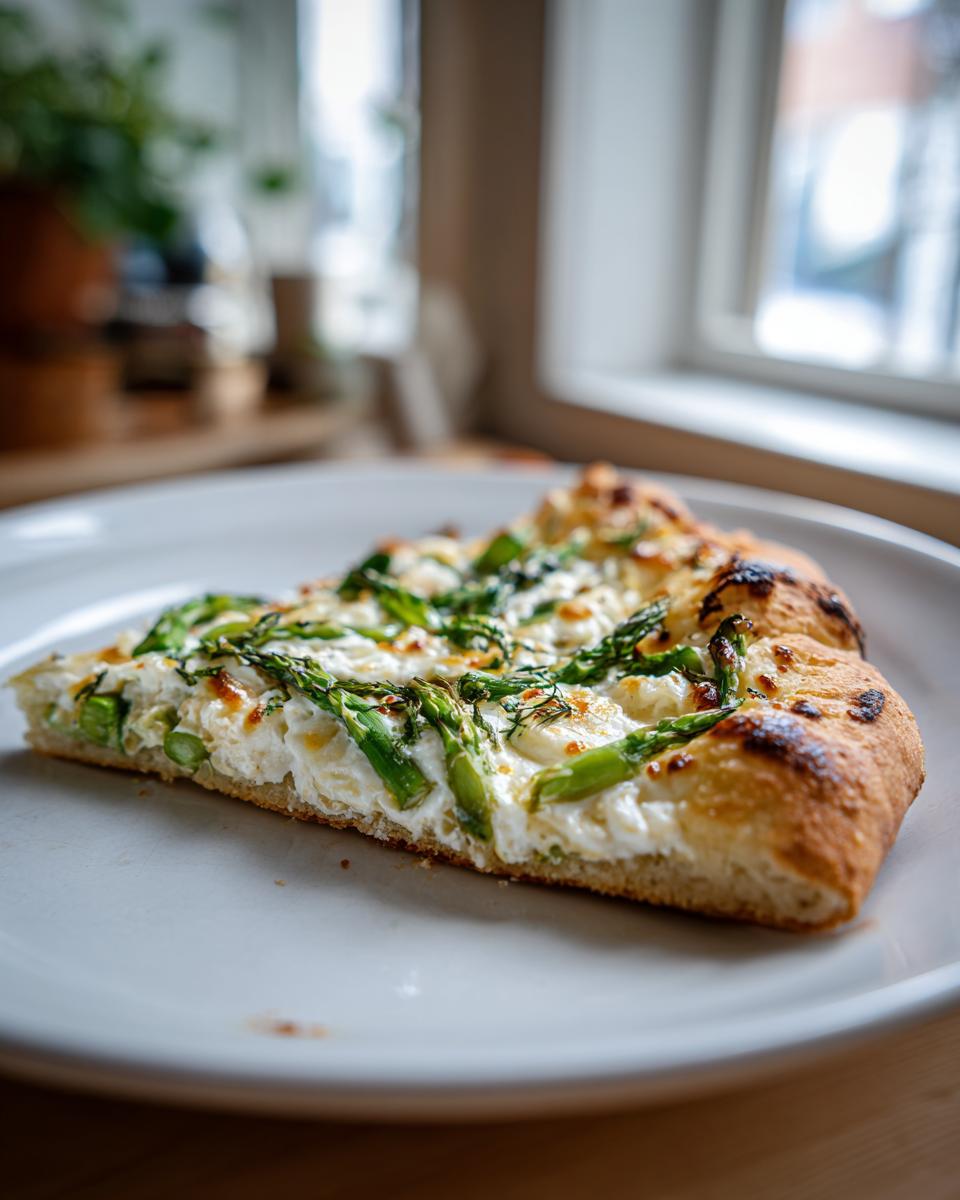 Ein Stück Spargel-Flammkuchen mit grünem Spargel und weißem Käsebelag auf einem hellen Teller.