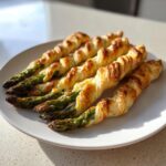Fünf goldbraun gebackene Spargel im Blätterteig mit Frischkäse auf einem weißen Teller.