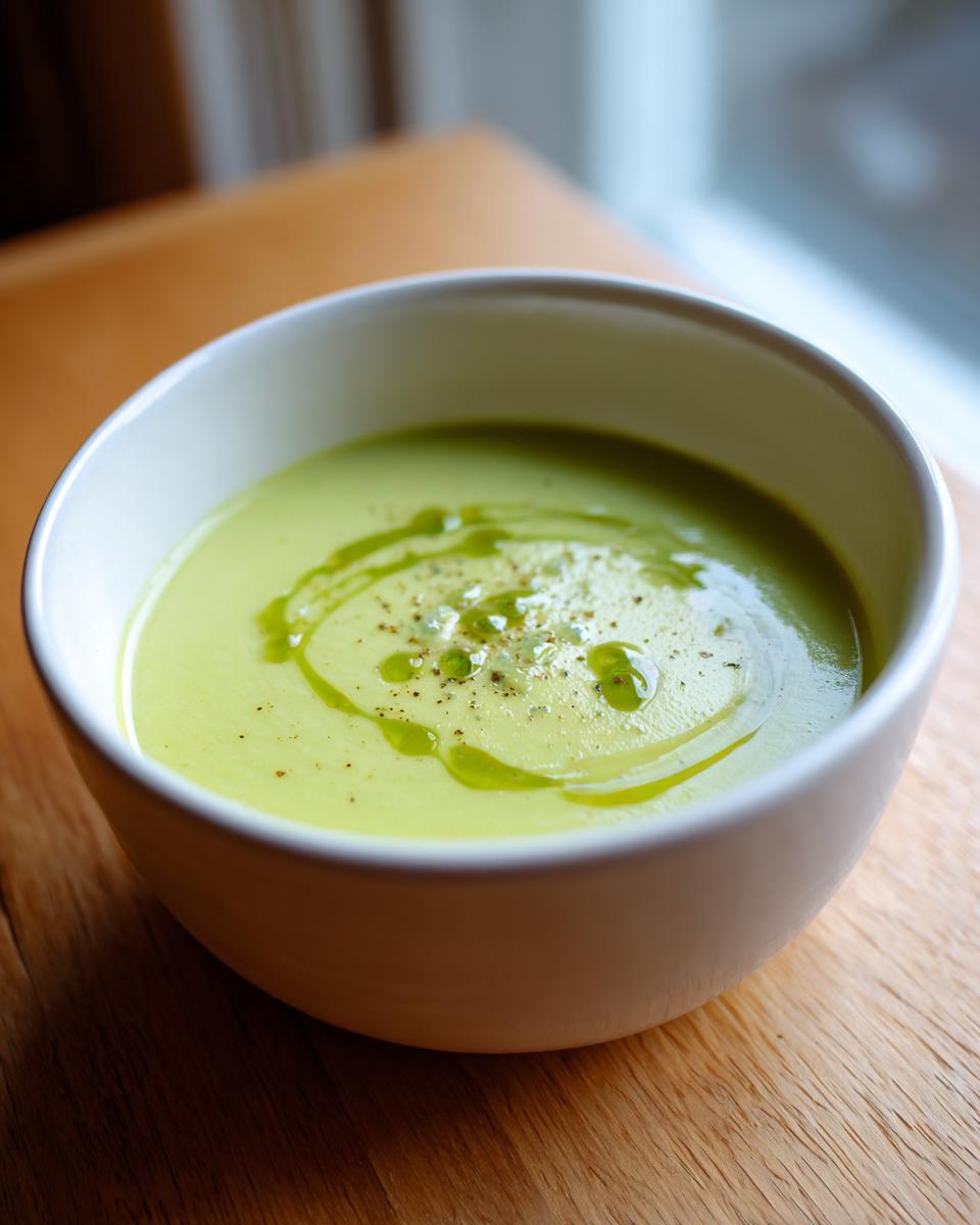 Eine Schale cremiger, hellgrüner Spargelcremesuppe aus Spargelschalen, garniert mit Öl und Pfeffer.