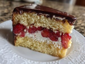Nahaufnahme eines Stücks Erdbeer-Donauwelle mit hellem Biskuit, Sahne und frischen Erdbeeren, bedeckt mit dunkler Schokolade.
