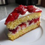 Nahaufnahme eines saftigen Stücks Erdbeertorte mit Biskuitboden, Sahne und glasierten Erdbeeren.