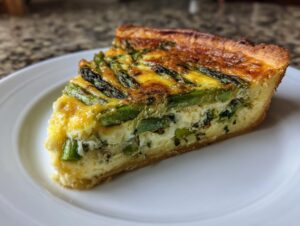 Ein großes Stück Knusprige Spargelquiche mit grünem Spargel und goldgelber Füllung auf einem weißen Teller.