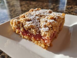 Ein Stück saftiger Rhabarber-Crumble mit knuspriger Streuseldecke und Puderzucker.