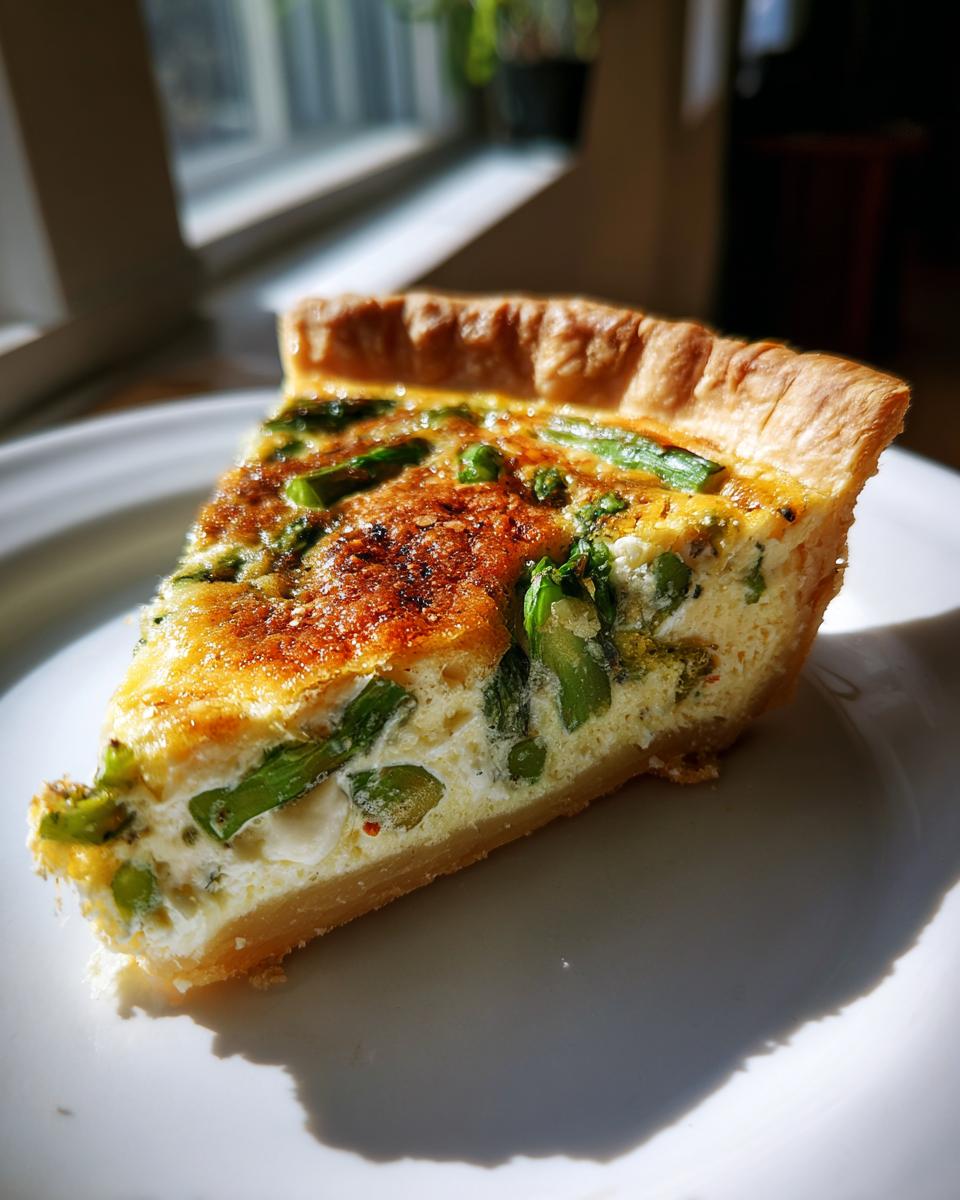 Ein Stück selbstgemachte Spargel-Quiche mit grünem Spargel in einer cremigen Ei-Füllung auf einem weißen Teller.