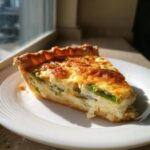 Nahaufnahme eines cremigen Stücks Spargel-Quiche mit goldbraun gebackener Kruste auf einem weißen Teller.